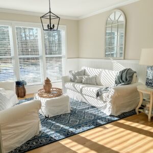 sunny white living room with slipcovered sofas and a coastal navy blue rug and rattan tray